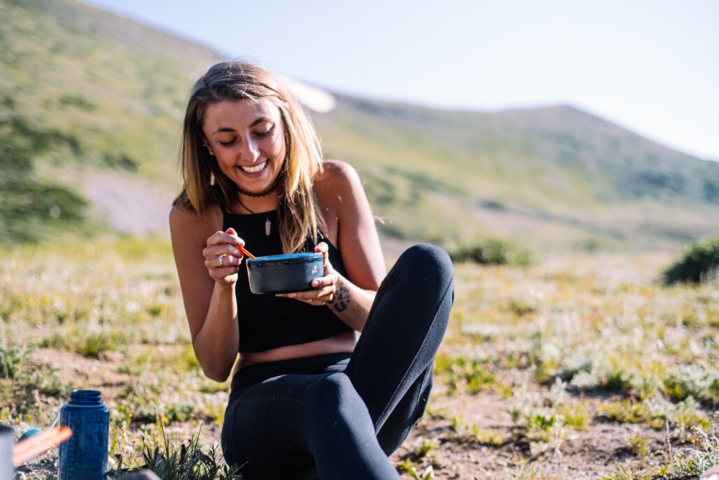 a girl sitting in nature enjoying a meal out of Tupperware.