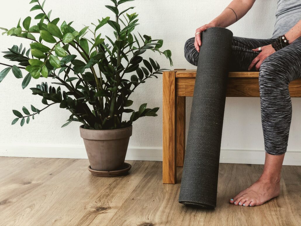 A woman sitting on a bench next to a plant with her yoga mat