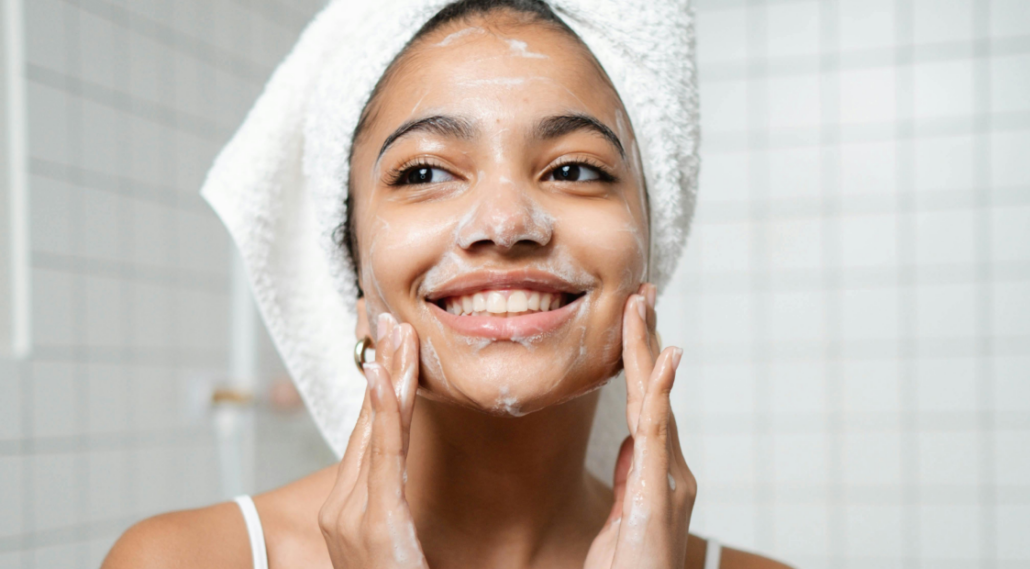 A girl putting on skin care products while smiling in the bathroom.